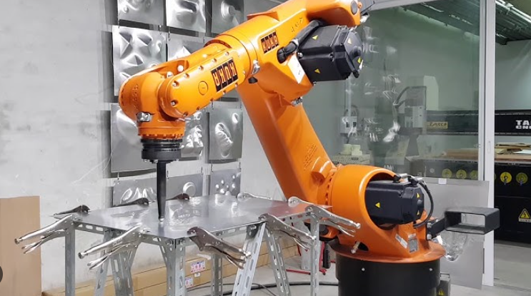 A robot arm pressing a tool into a clamped metal sheet.