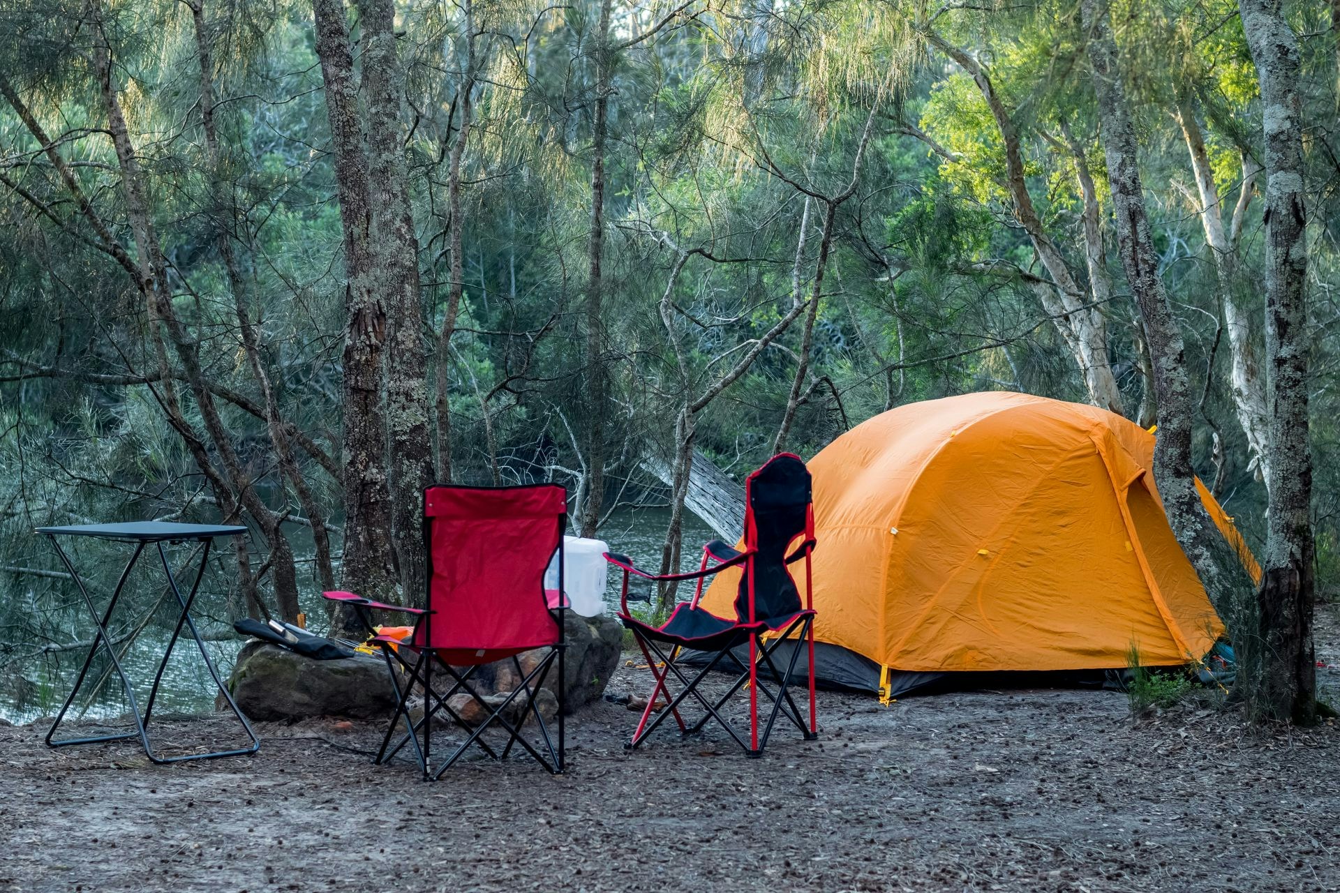 Photograph of a camping tent and chairs in a forest.