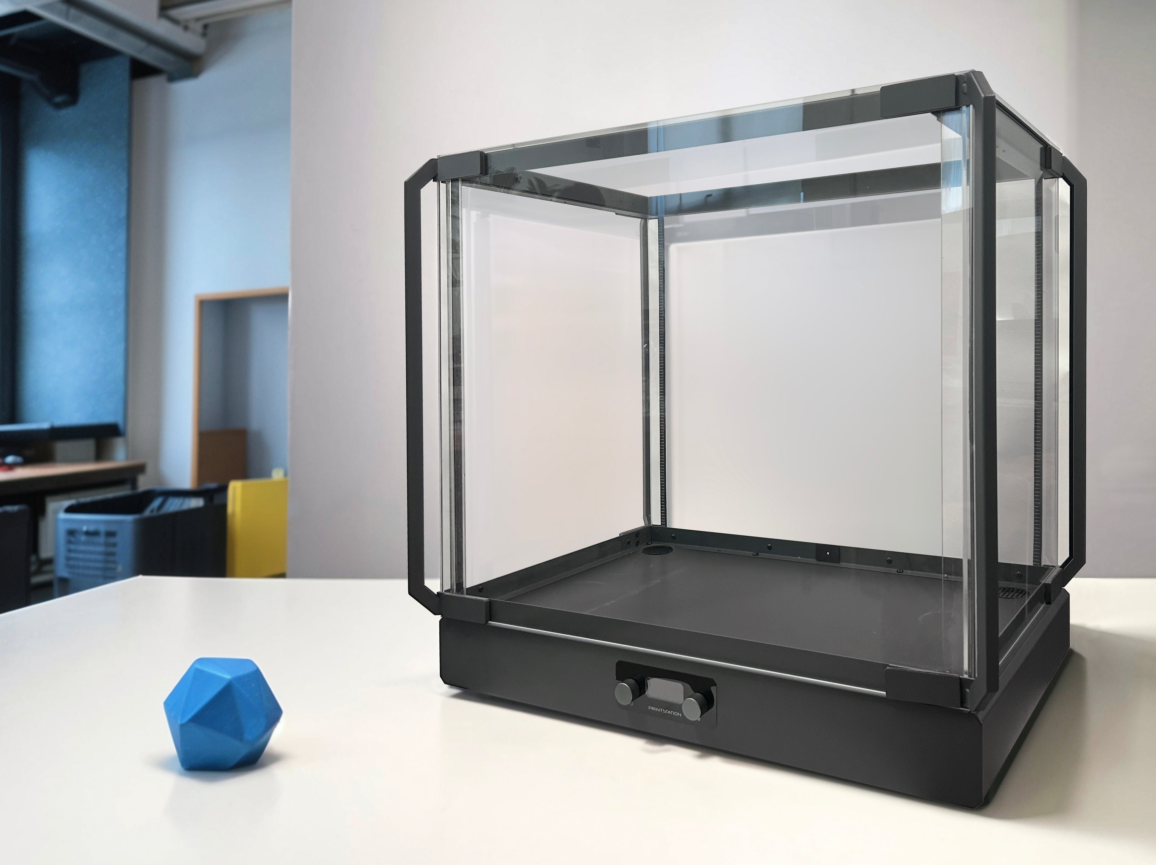 A clear 3D printer enclosure on a desk next to a printed part