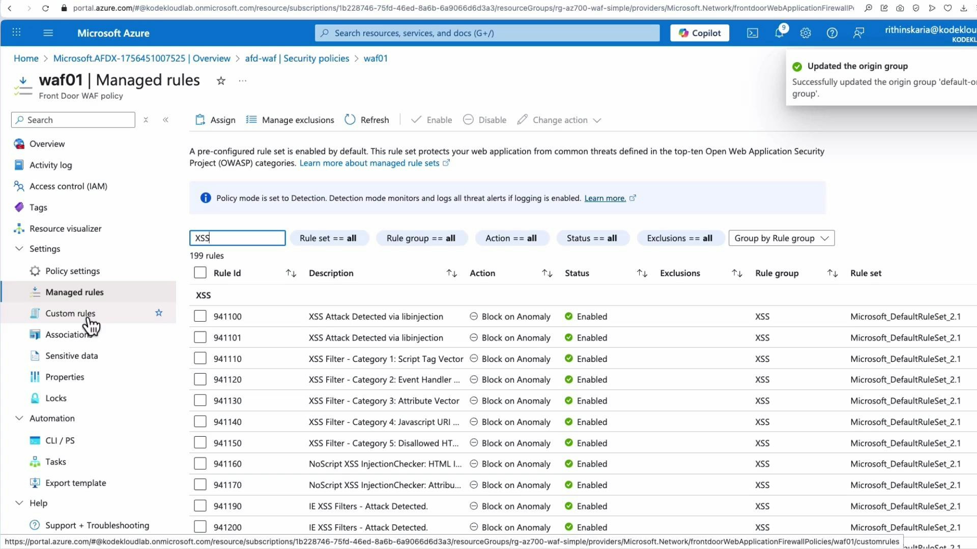 A screenshot of the Microsoft Azure portal open to a Front Door WAF policy page titled "waf01 | Managed rules," showing a list of XSS-related managed rules, their IDs, actions (e.g., Block on Anomaly) and enabled statuses. The left menu highlights "Managed rules" and "Custom rules," and a notification in the top-right says the origin group was updated.