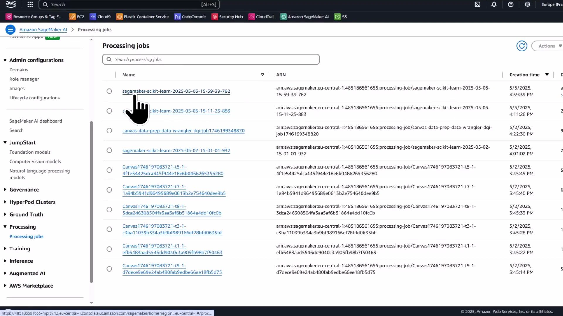 A screenshot of the Amazon SageMaker console showing the "Processing jobs" list with job names, ARNs, and creation times. A hand-shaped cursor is pointing at one of the scikit-learn processing jobs.