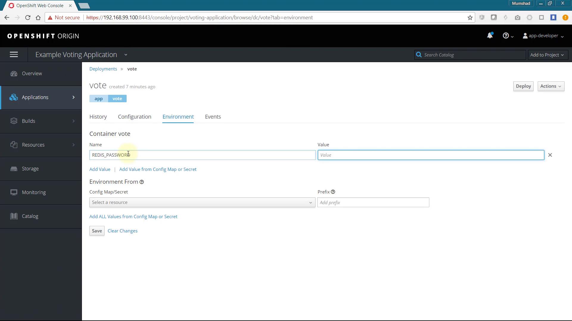 A screenshot of the OpenShift Origin web console showing the "Example Voting Application" deployments page on the Environment tab for a container named "vote." The form displays an environment variable entry for REDIS_PASSWORD with a blank Value field and options to add values from a ConfigMap/Secret.