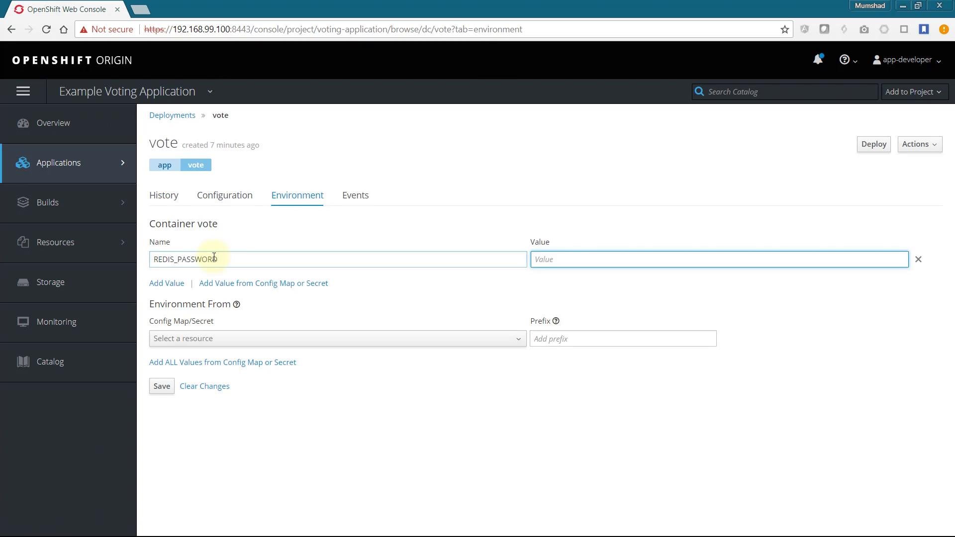 A screenshot of the OpenShift Origin web console showing the "Example Voting Application" deployments page on the Environment tab for a container named "vote." The form displays an environment variable entry for REDIS_PASSWORD with a blank Value field and options to add values from a ConfigMap/Secret.
