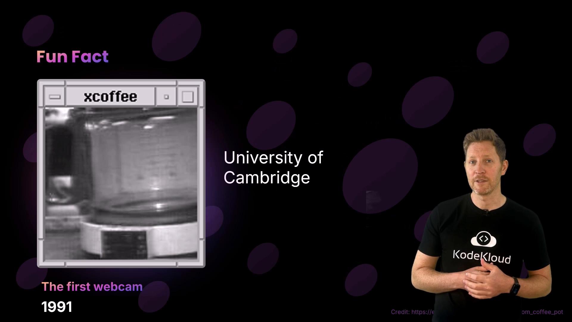 A presentation slide about the University of Cambridge’s “first webcam” (1991) showing a small grayscale webcam image of a coffee pot labeled “xcoffee” on the left. A presenter in a KodeKloud t‑shirt stands on the right against a dark background.