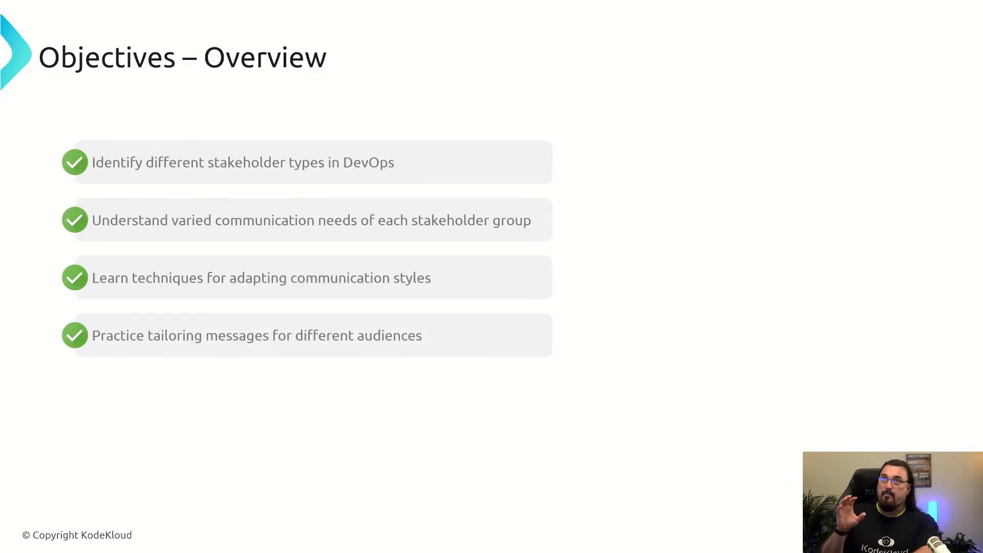 A presentation slide titled "Objectives – Overview" lists four checked learning goals about DevOps stakeholder types and communication (identify stakeholders, understand needs, adapt styles, tailor messages). A small video thumbnail of the presenter appears in the bottom-right.