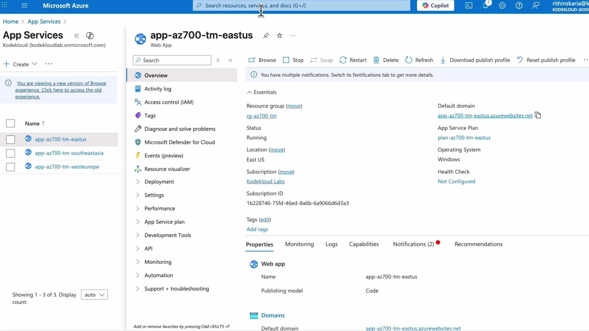 Screenshot of the Microsoft Azure portal showing the App Services overview for a web app named "app-az700-tm-eastus," with essentials like resource group, status (Running), location (East US) and default domain. The left pane lists other app instances and navigation/settings options.
