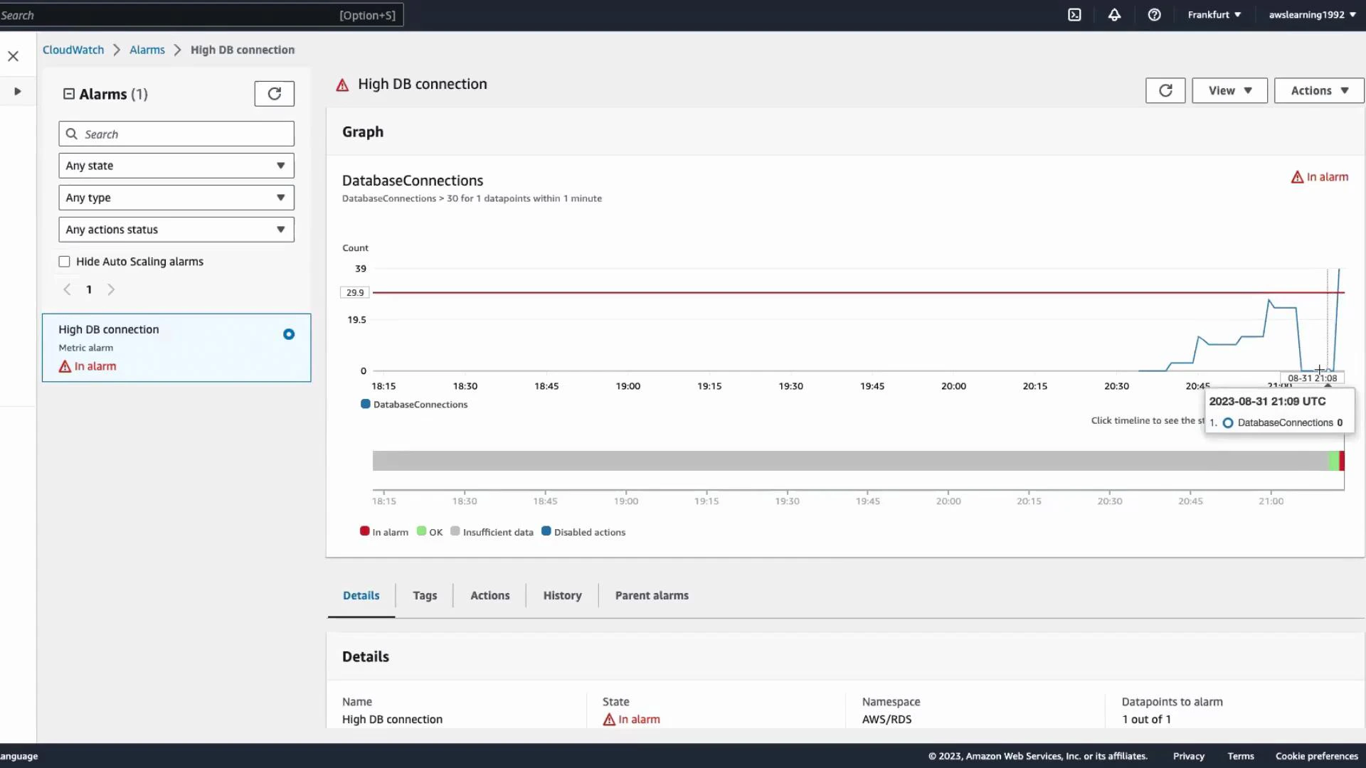 A screenshot of the AWS CloudWatch Alarms page showing a "High DB connection" metric alarm marked "In alarm." The graph displays DatabaseConnections spiking above the threshold line.