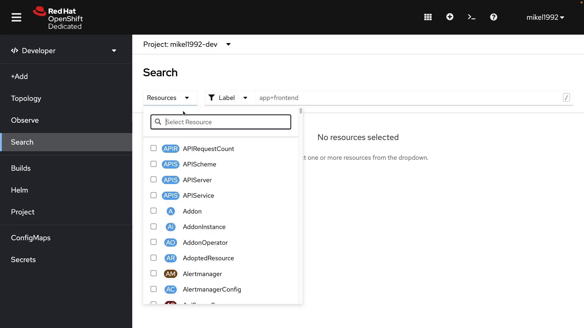 A screenshot of the Red Hat OpenShift Dedicated developer console showing the Search page for project "mikel1992-dev" with the Resources dropdown expanded, listing resource types like APIRequestCount, APIScheme, APIServer, and more. The sidebar navigation is visible and a label filter "app=frontend" is applied while the main pane reads "No resources selected."