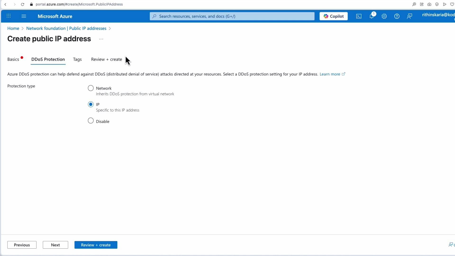 A screenshot of the Microsoft Azure portal showing the "Create public IP address" workflow on the "DDoS Protection" tab, with radio options for Network, IP (selected), and Disable. The page includes navigation breadcrumbs, a search bar, and buttons for Previous/Next/Review + create.