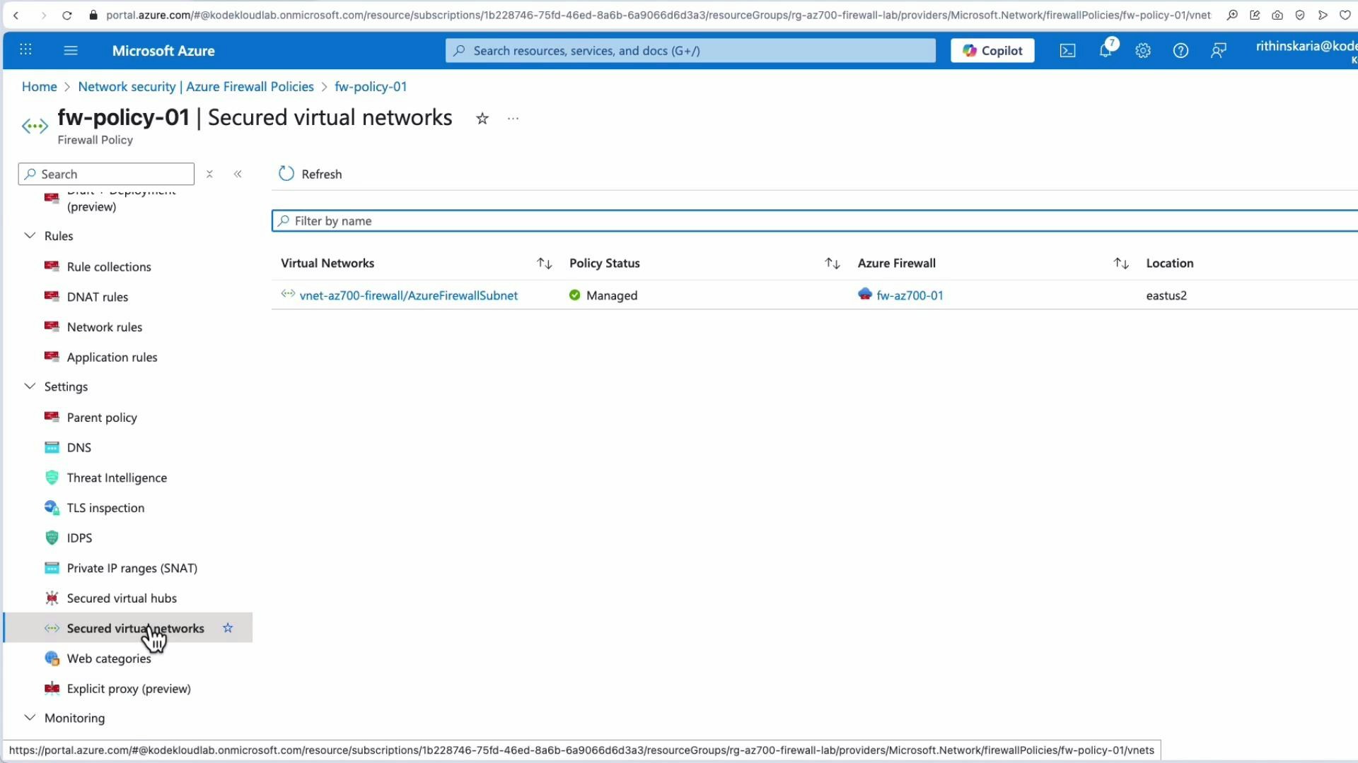 A screenshot of the Microsoft Azure portal showing a firewall policy page titled "fw-policy-01 | Secured virtual networks." The page lists a virtual network (vnet-az700-firewall/AzureFirewallSubnet) with its policy status as Managed and the associated Azure Firewall and location.