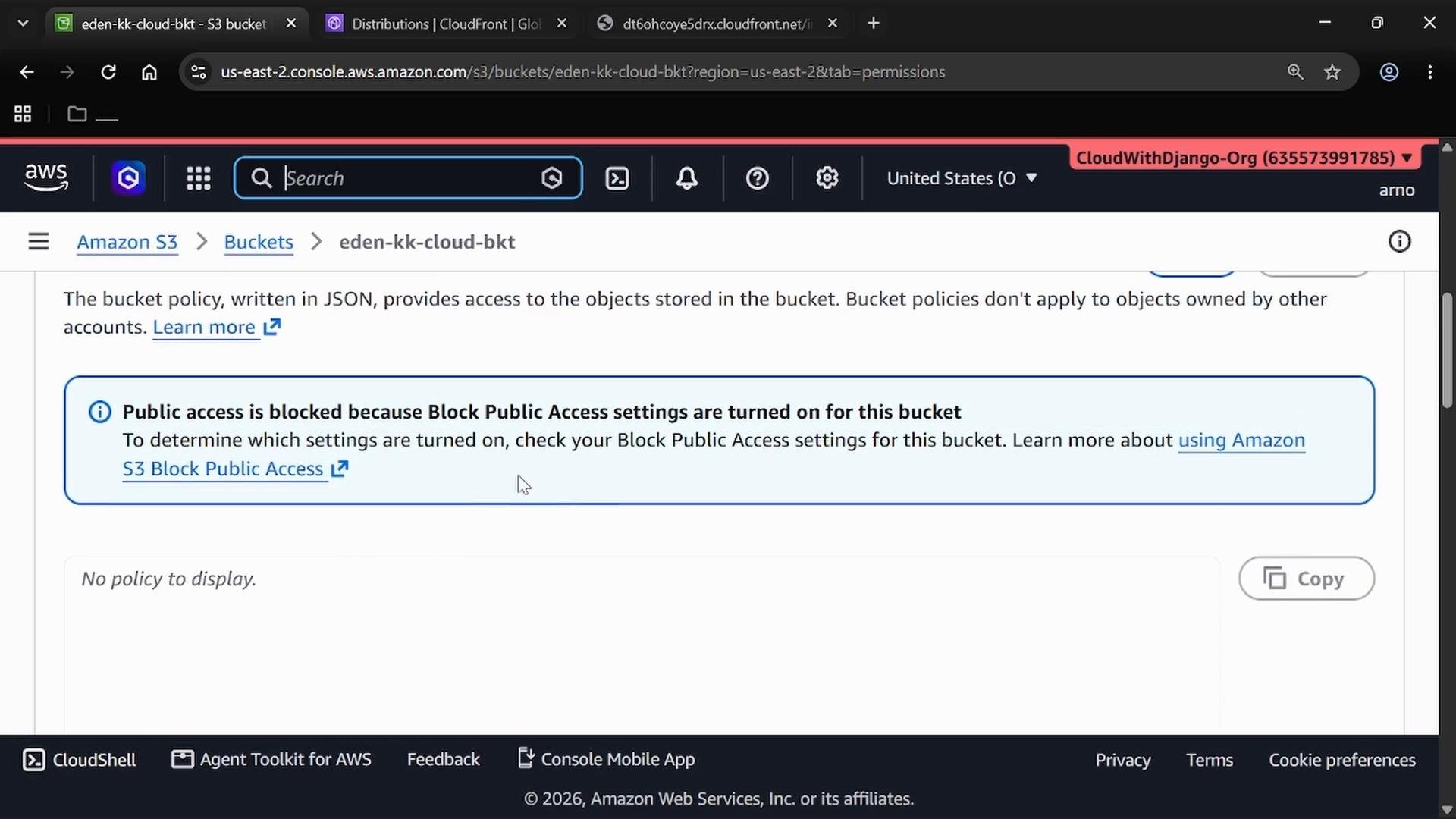 A screenshot of the Amazon S3 console on a bucket permissions page showing a blue banner that "Public access is blocked because Block Public Access settings are turned on for this bucket." The page also shows "No policy to display."