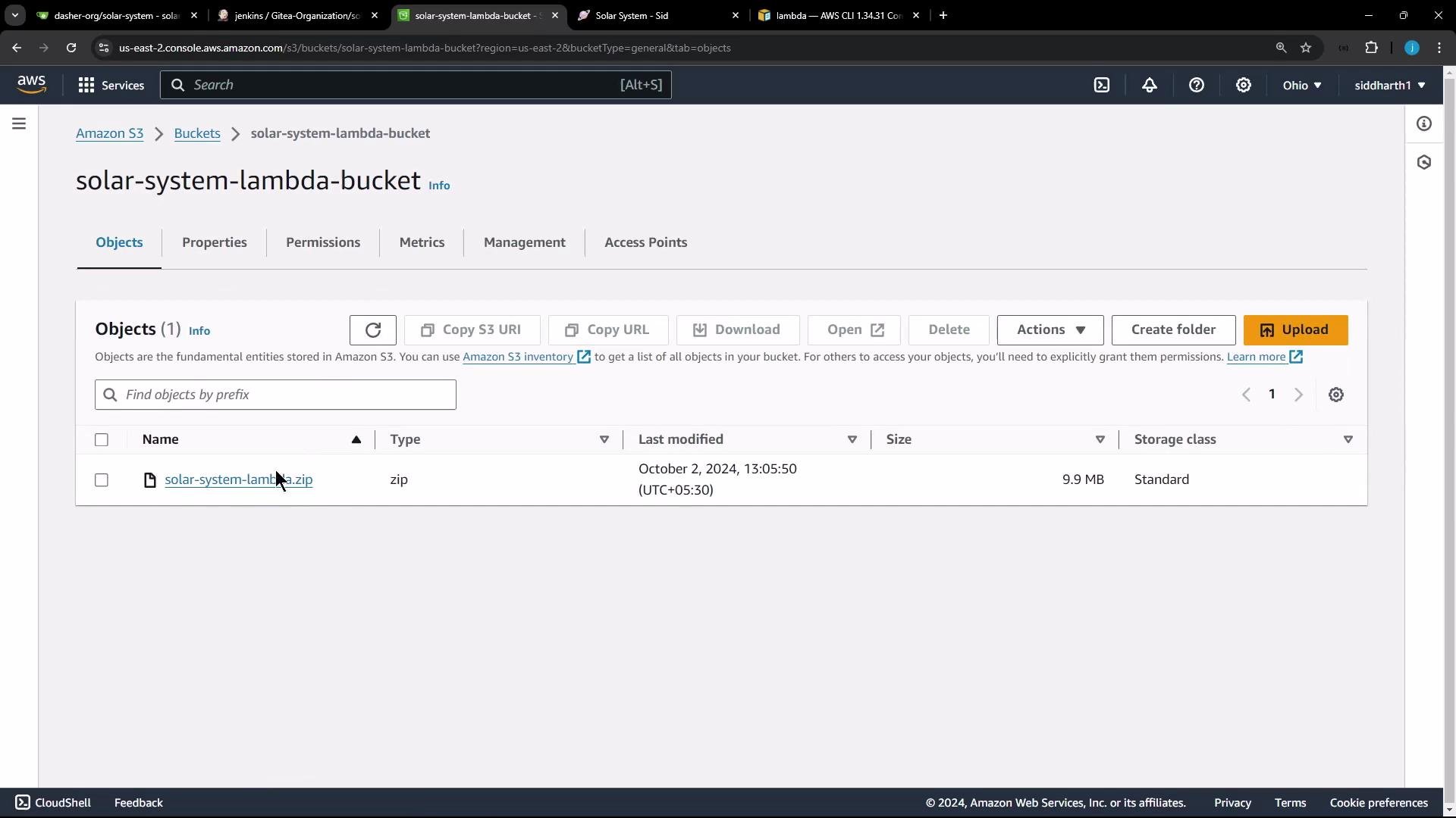 A screenshot of the AWS S3 console showing the bucket "solar-system-lambda-bucket" with a single object: "solar-system-lambda.zip" (9.9 MB) and its last modified timestamp. The S3 toolbar (Upload, Actions, Copy URL, etc.) and bucket tabs (Objects, Properties, Permissions) are also visible.