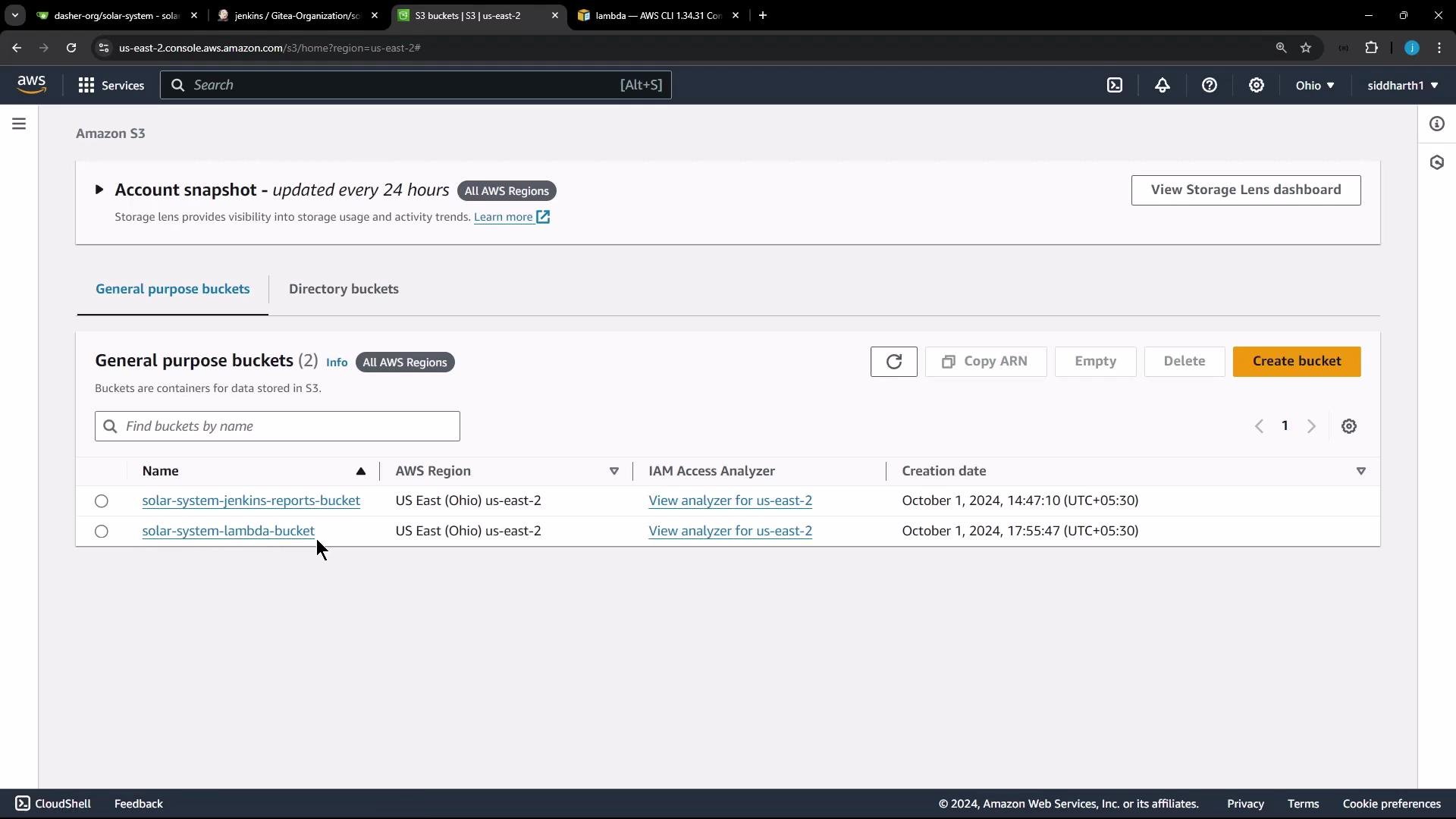 A screenshot of the AWS S3 console showing the "General purpose buckets" list with two buckets: "solar-system-jenkins-reports-bucket" and "solar-system-lambda-bucket" in the US East (Ohio) us-east-2 region. The page shows creation dates, IAM Access Analyzer links, and controls like "Create bucket."