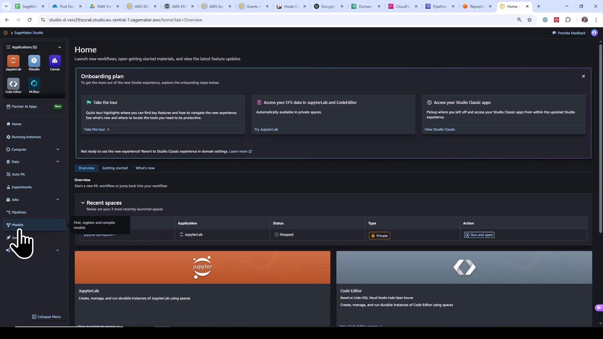 A dark-themed screenshot of the AWS SageMaker Studio Home dashboard showing onboarding panels, navigation sidebar (JupyterLab, RStudio, Code Editor, etc.), and a "Recent spaces" section. A large pointer/cursor is clicking the "Models" item in the left sidebar.