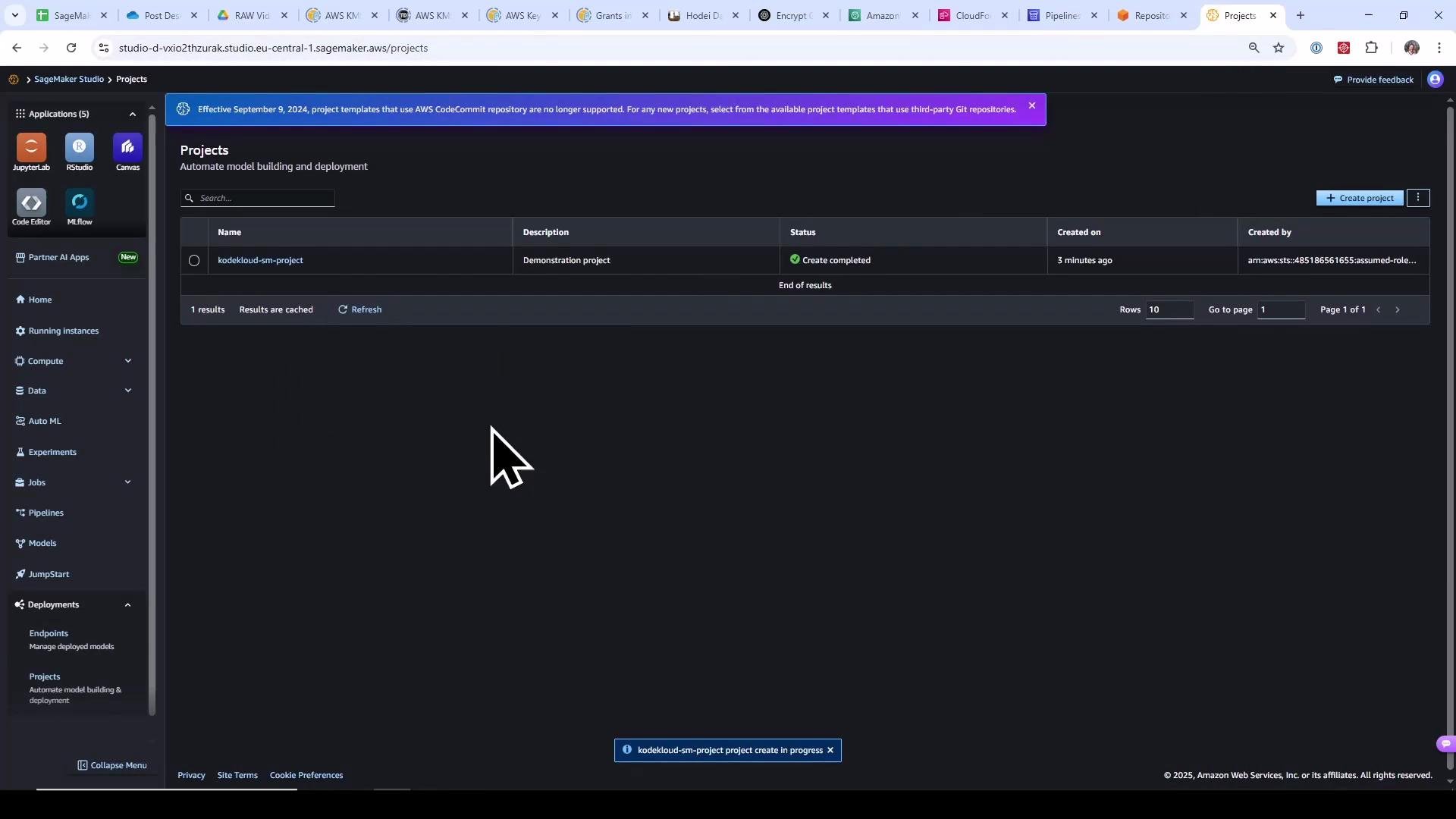 A screenshot of the AWS SageMaker Studio "Projects" page showing a project named "kodekloud-sm-project" with status "Create completed." The dark-themed interface includes a left navigation pane (JupyterLab, RStudio, etc.) and a large mouse cursor visible over the workspace.