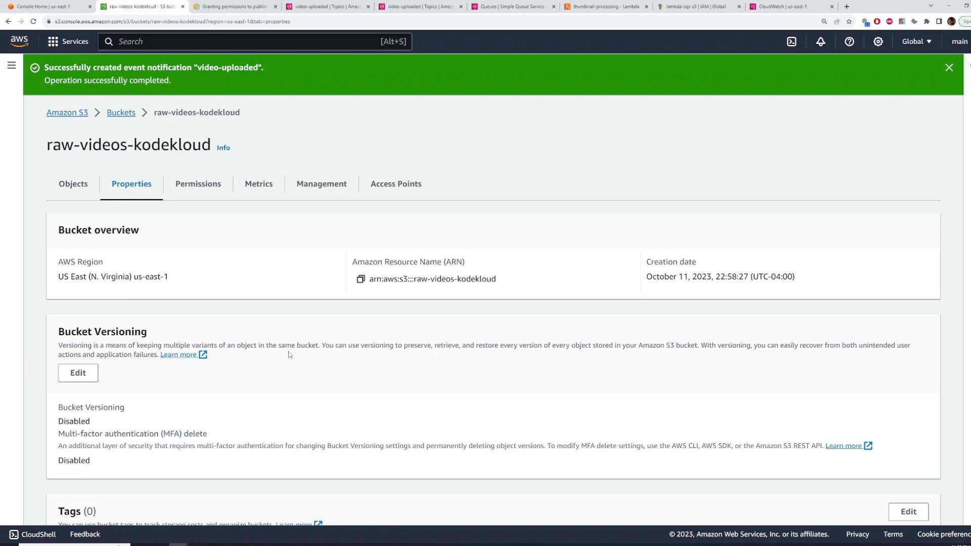 Screenshot of the AWS S3 console showing the Properties page for the bucket "raw-videos-kodekloud" with bucket overview and versioning settings. A green banner at the top notes a successful creation of the "video-uploaded" event notification.
