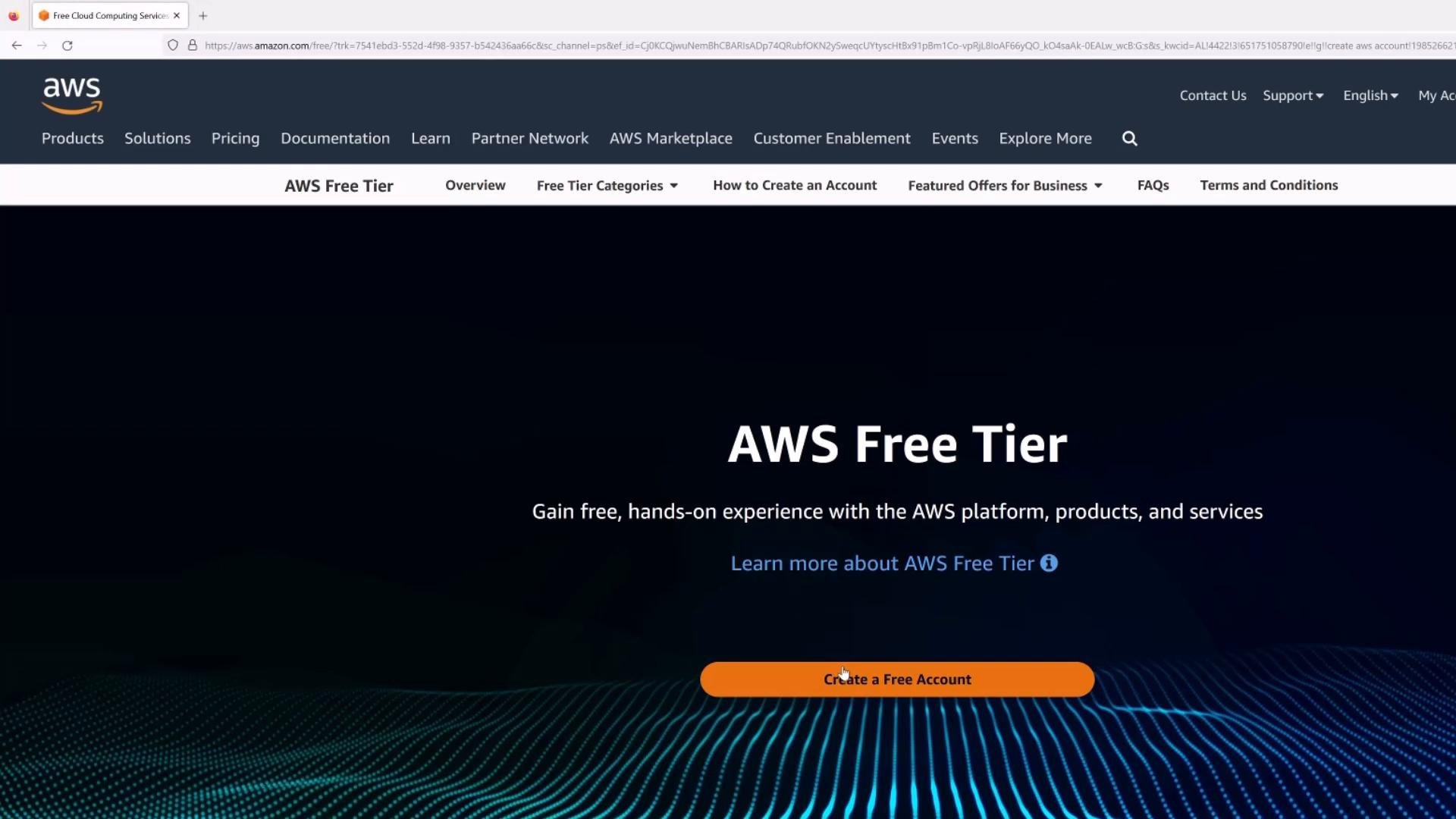 A screenshot of the AWS Free Tier webpage with the AWS logo and navigation links at the top, a large "AWS Free Tier" heading, and an orange "Create a Free Account" button. The page has a dark background with a blue wavy dotted pattern at the bottom.