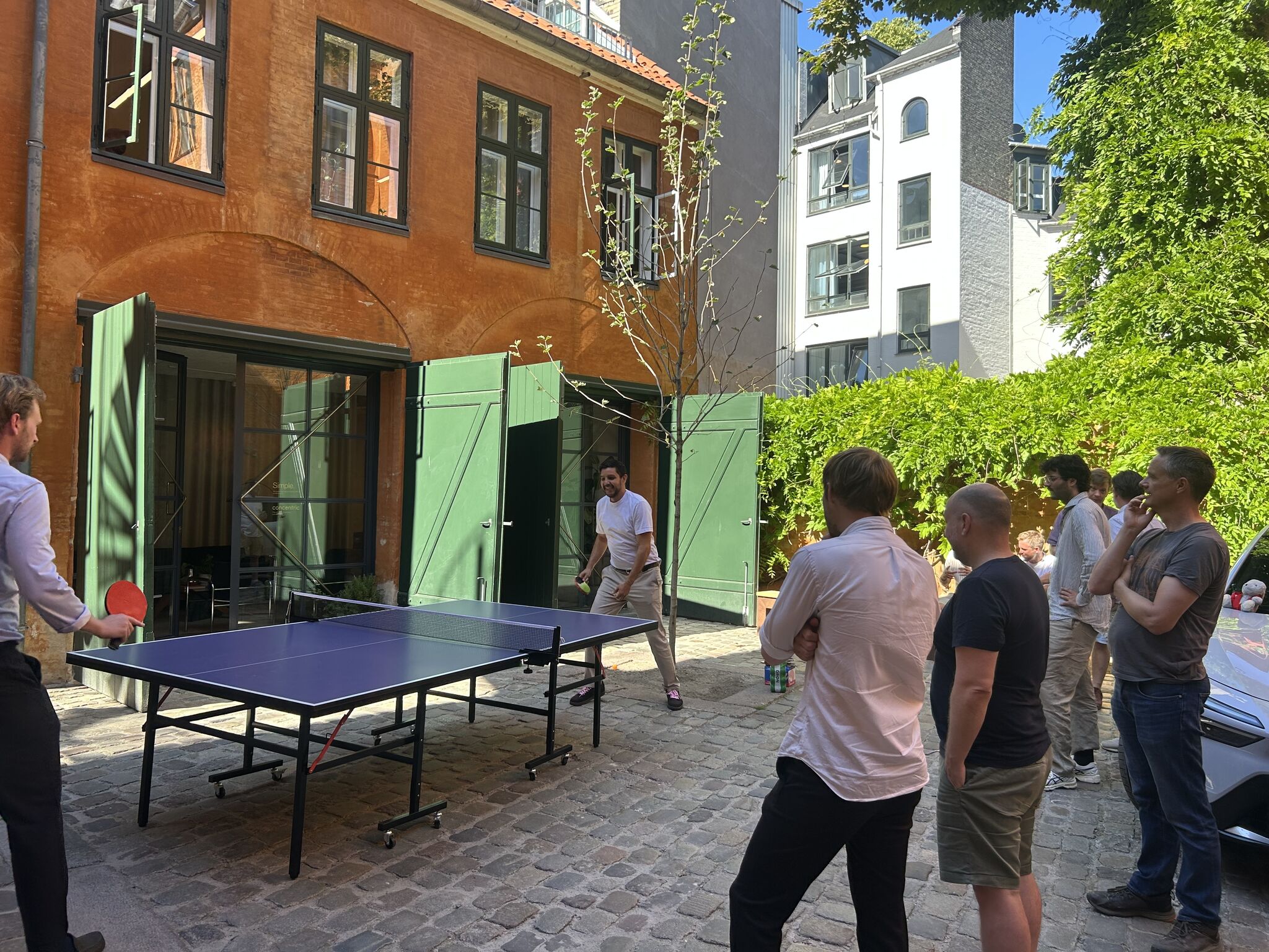 Community members playing table tennis in a sunny Copenhagen courtyard.