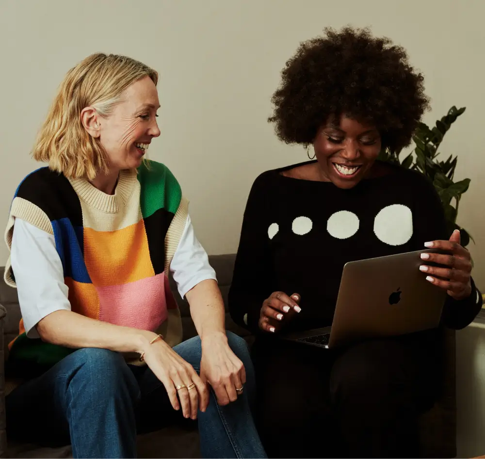Two colleagues sharing a smile while working together on a laptop.