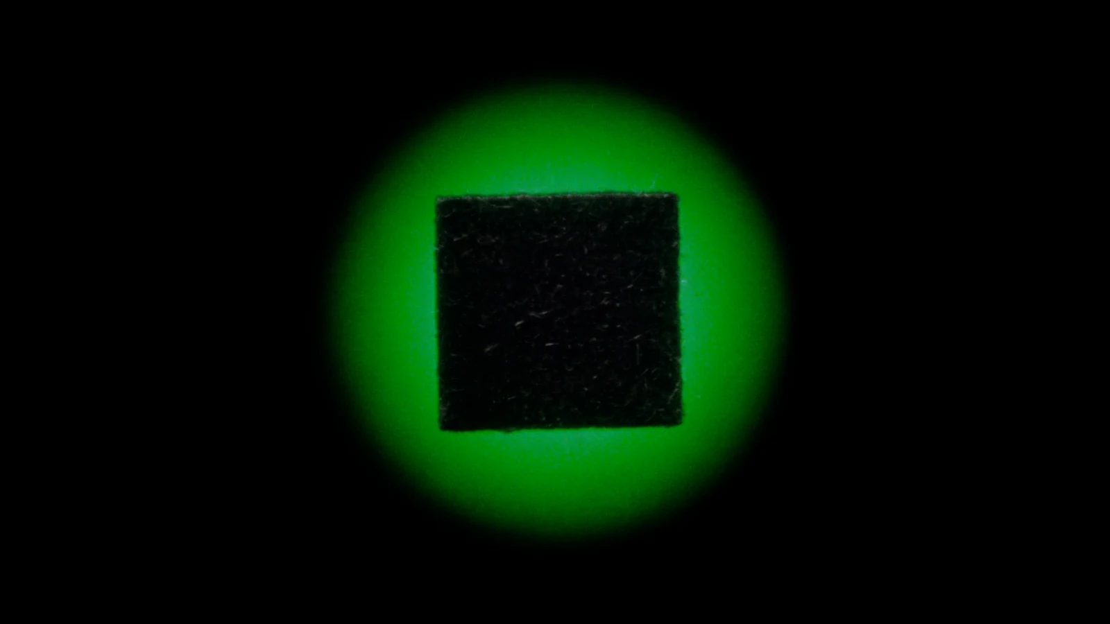 A matte cube held inside a ring of green light on a black background