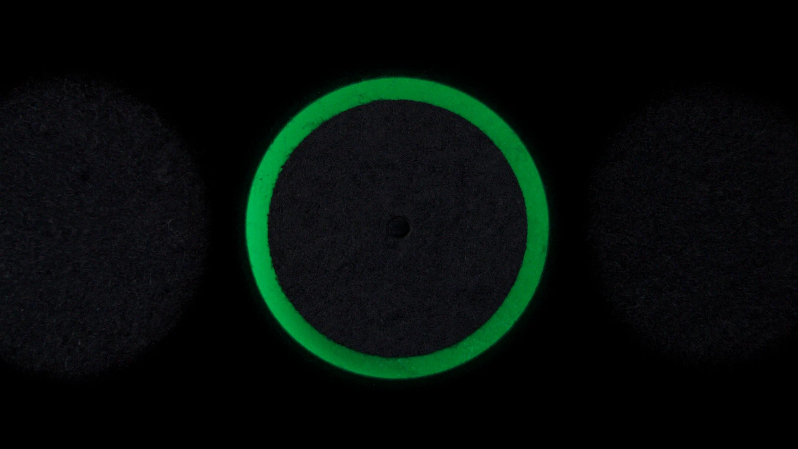 Plusieurs disques mats posés à plat sur un fond sombre, un seul cerné de vert