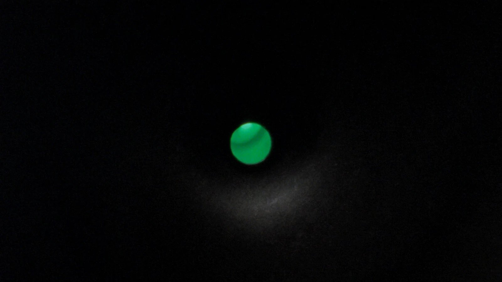 A small green sphere suspended at the centre of a vast matte surface