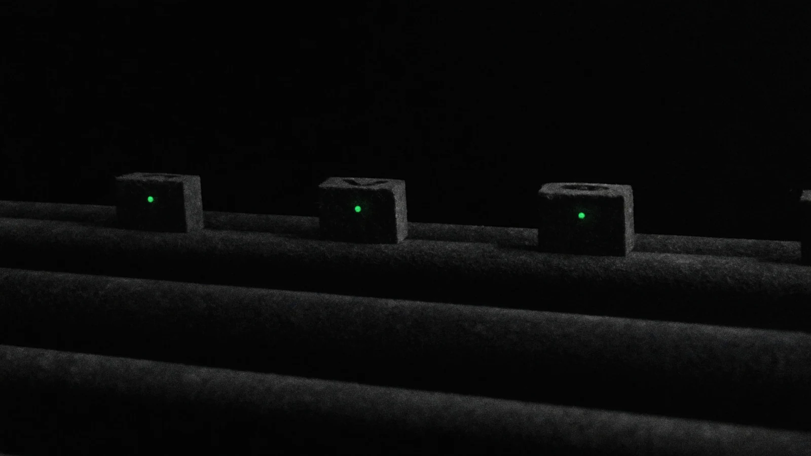 Small matte blocks resting on parallel rails on a black background, a green mark on each