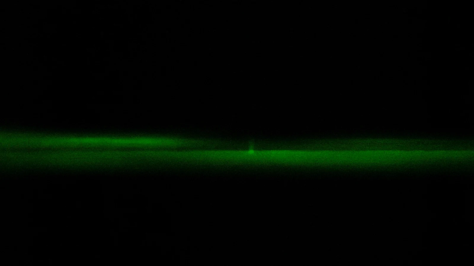 A long streak of green light shooting horizontally through the dark