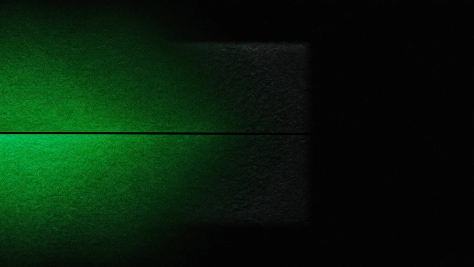 A green line of light sweeping across the face of a dark matte cube