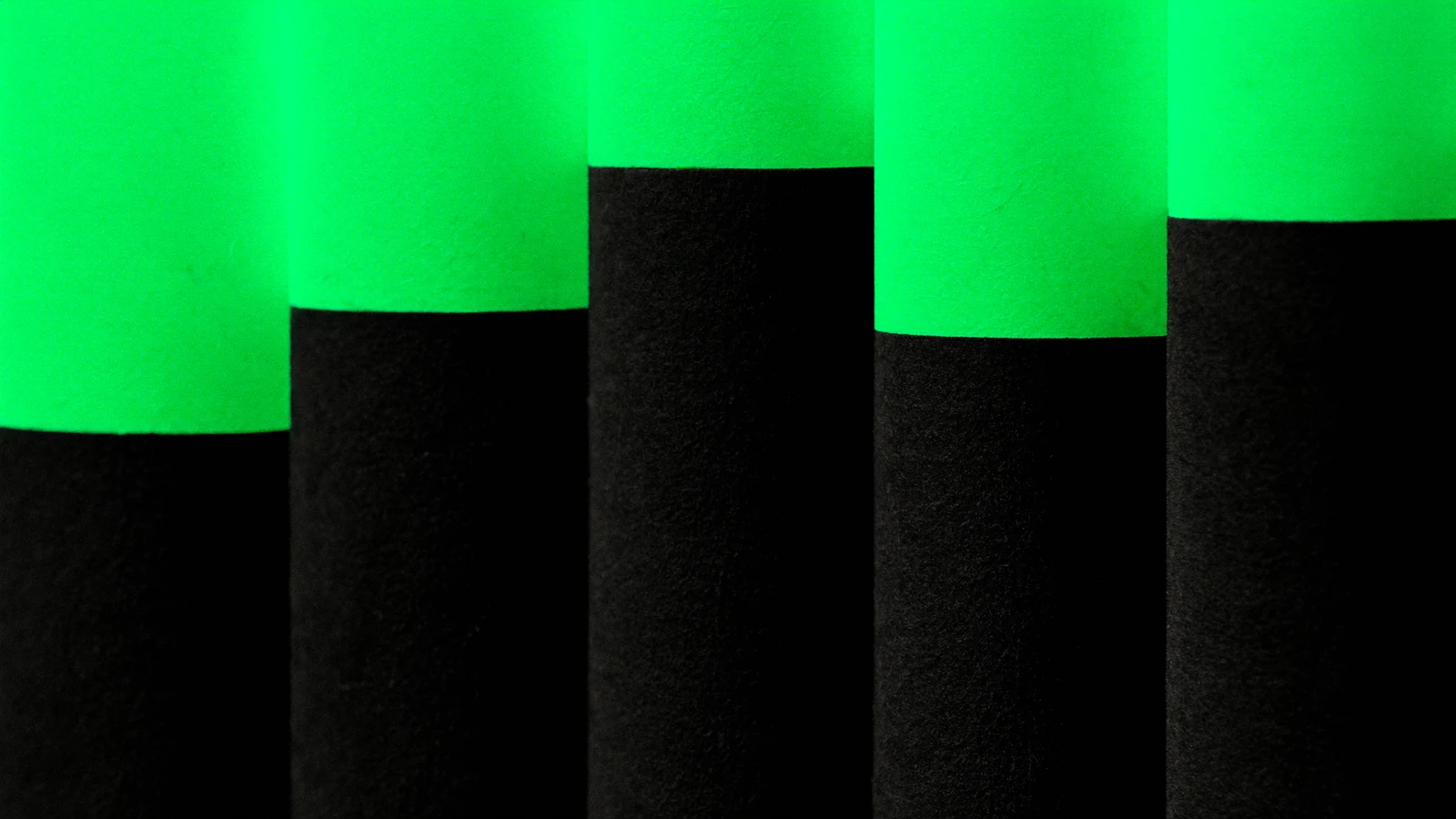 Five matt pillars of different heights, lit in green along their tops
