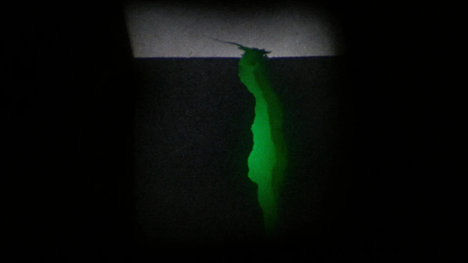 A dark matte cube with a crack across it, green light escaping from the split