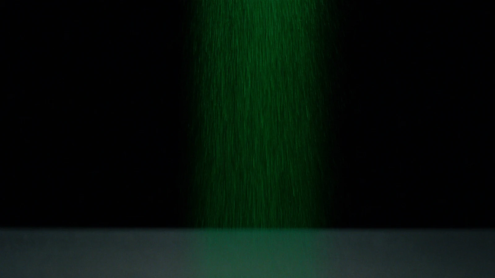 A column of very fine grain falling through the dark, lit in green