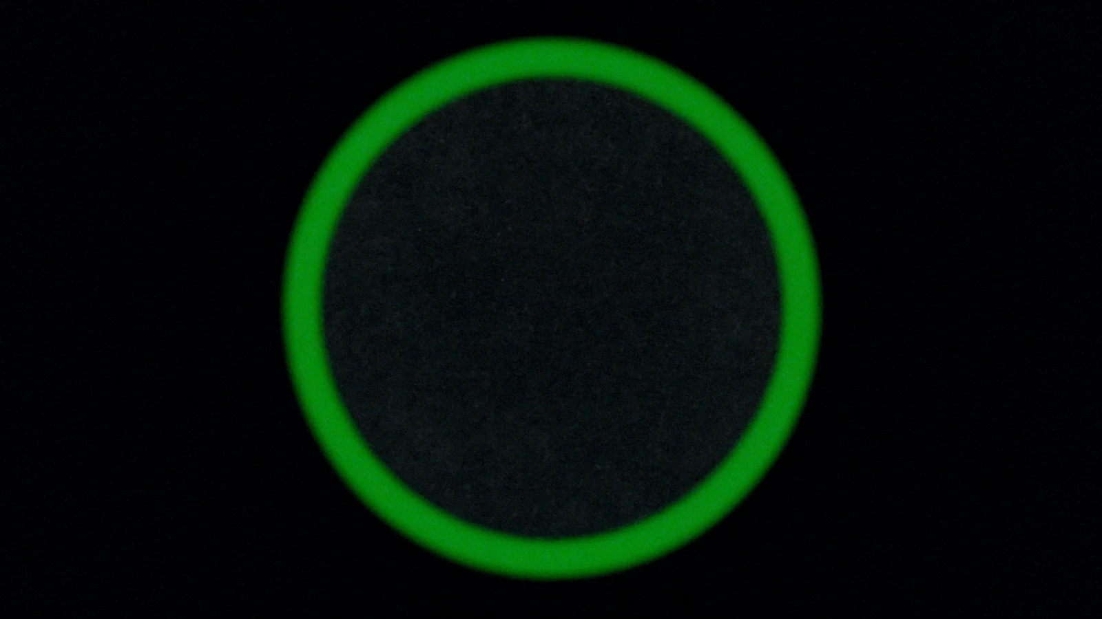 A dark matte disc surrounded by a continuous ring of green light