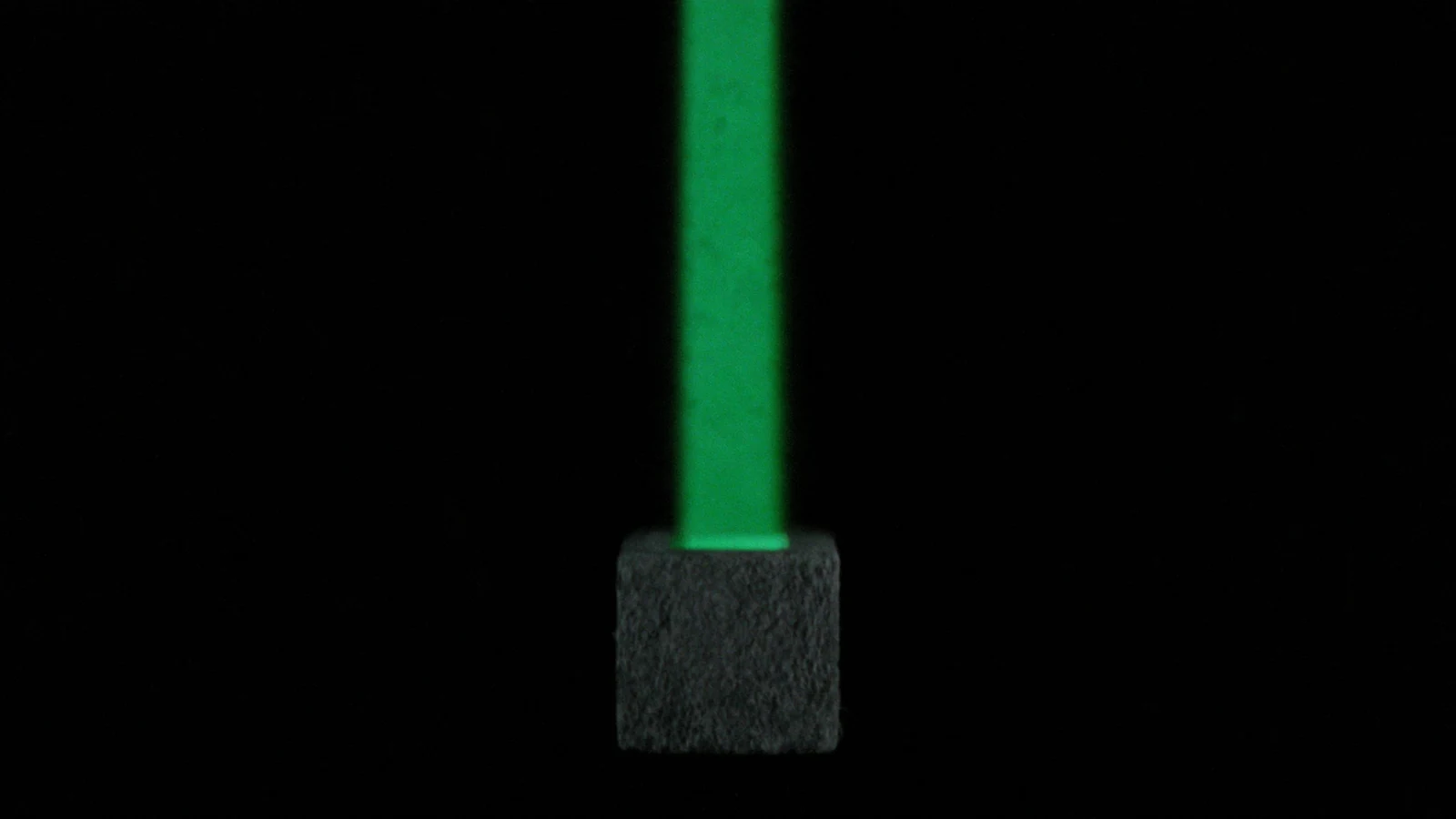 A matte cube standing alone under a very narrow beam of green light on a black background