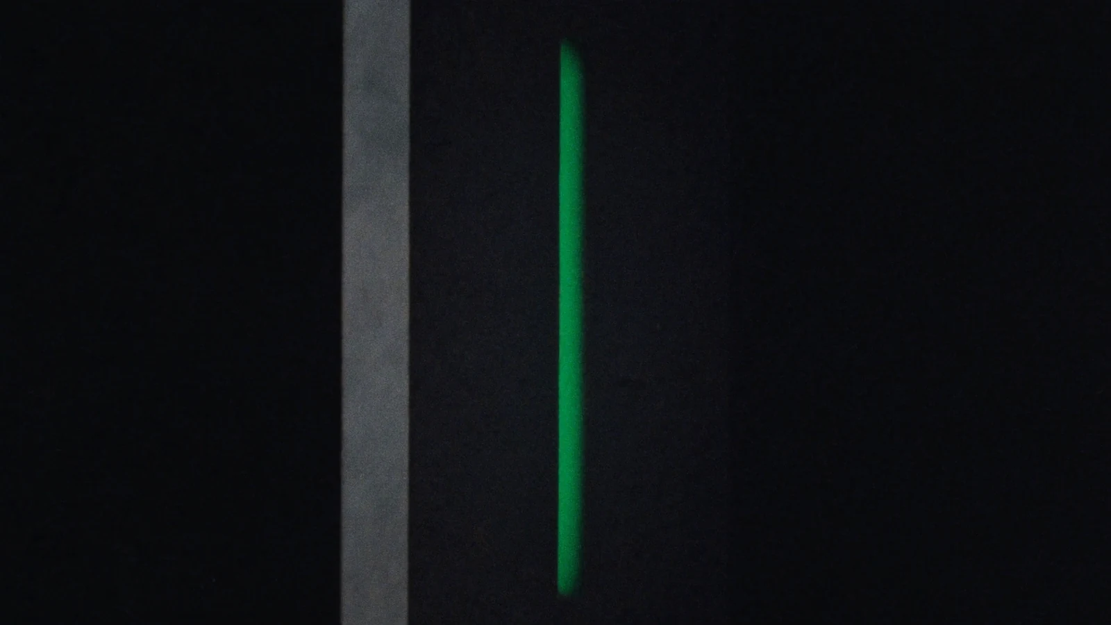 A narrow vertical slit of green light in a matte dark wall