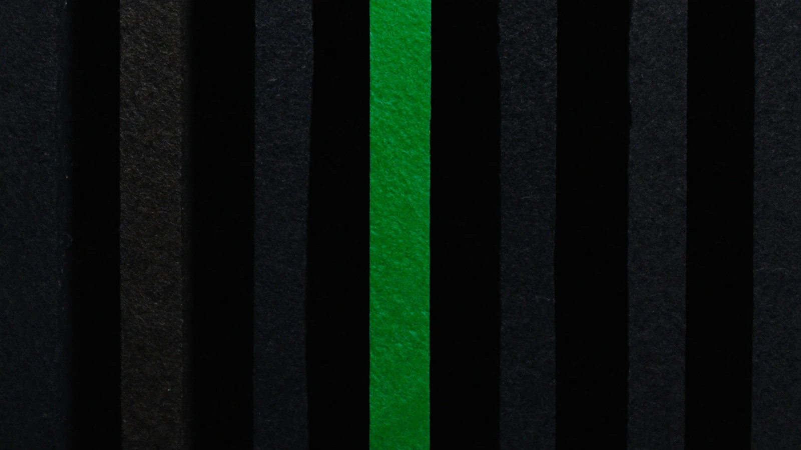 A line of matte tiles aligned in shadow, a single one lit in green