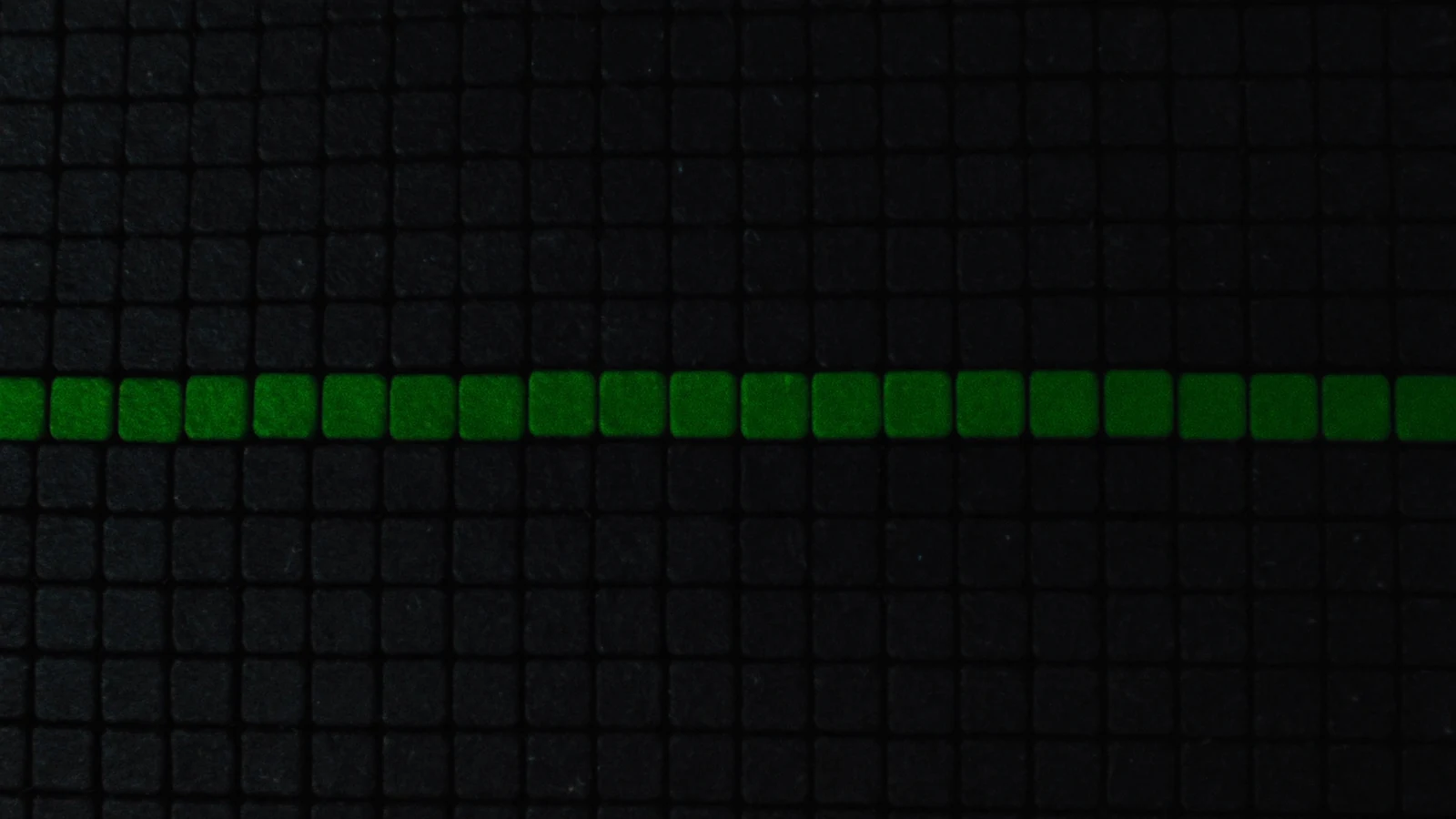 A grid of matt cubes crossed by a thin green beam lighting only one row