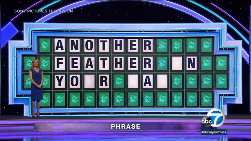 A Wheel of Fortune puzzle board showing 'ANOTHER FEATHER _N YO_R _A_' under the category PHRASE.