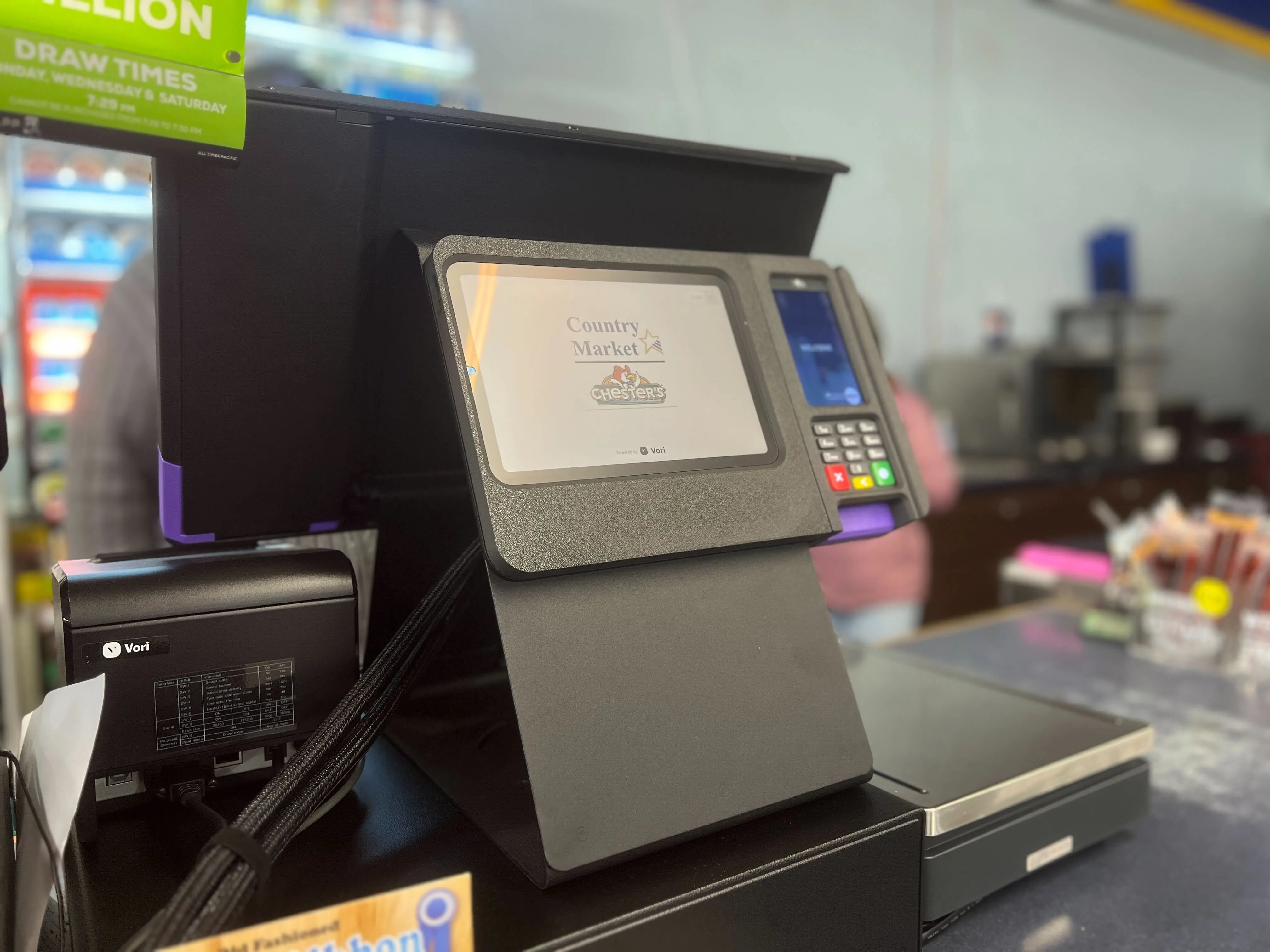 The shopper display mounted at a checkout lane, facing the shopper with the store logo on screen