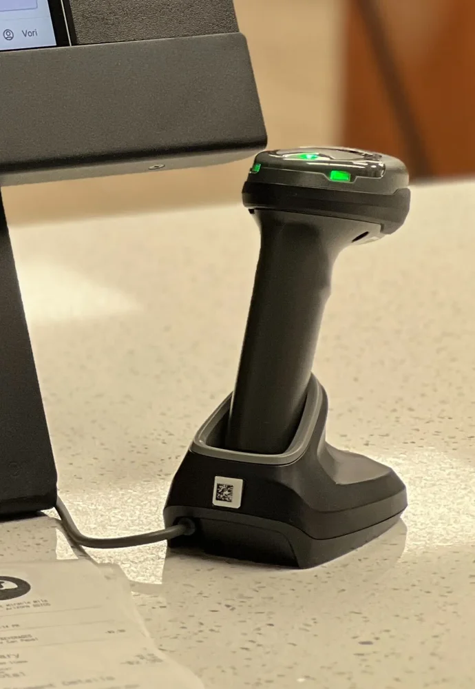 The handheld barcode scanner resting on its charging cradle, with green status lights on top