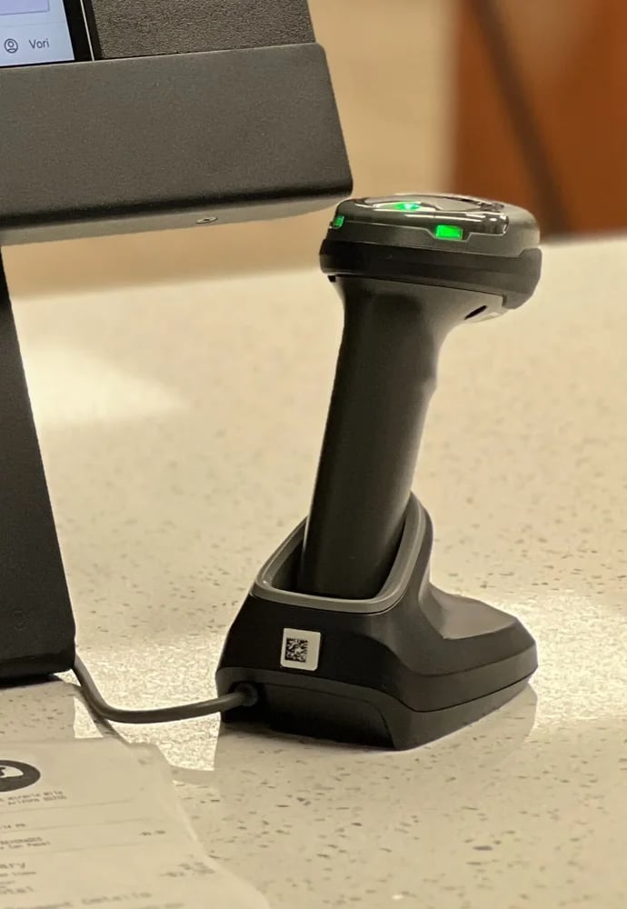 The handheld barcode scanner resting on its charging cradle, with green status lights on top